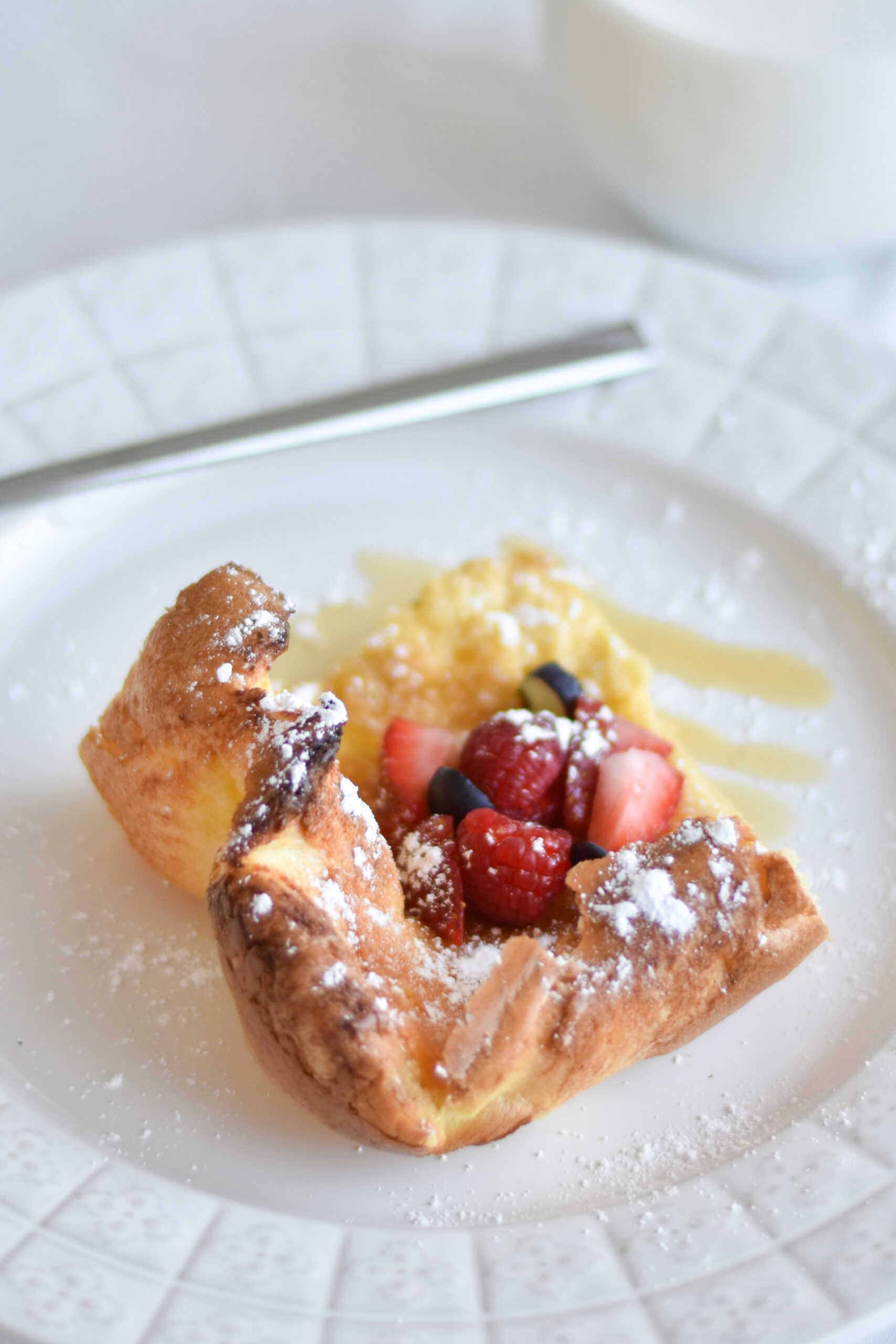 baked German pancake puffed and golden served on a plate with powdered sugar, berries, and syrup