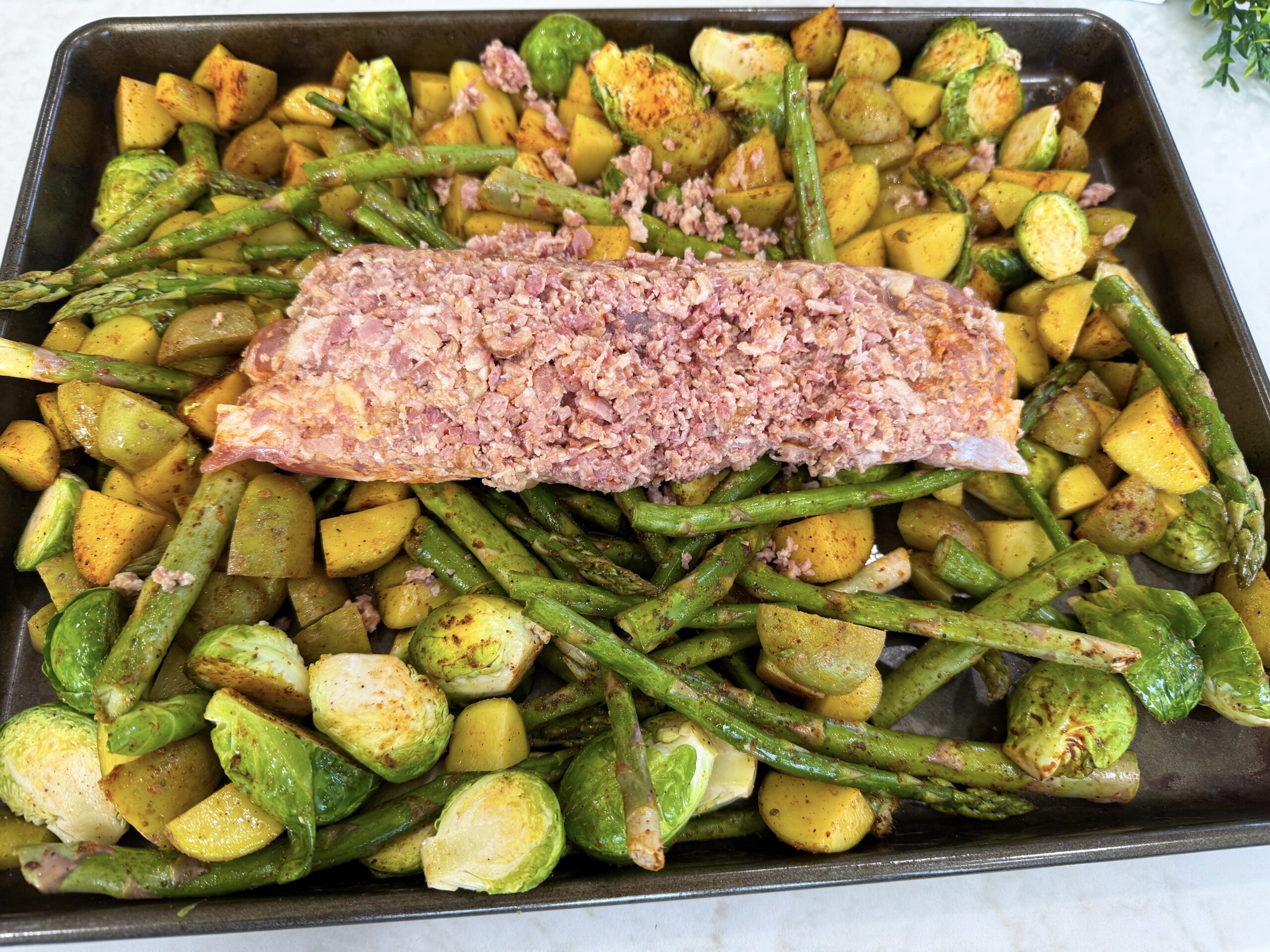 vegetables spread on a sheet pan with pork tenderloin in the center