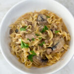 Cooked egg noodles and ground turkey for stroganoff and white bowl