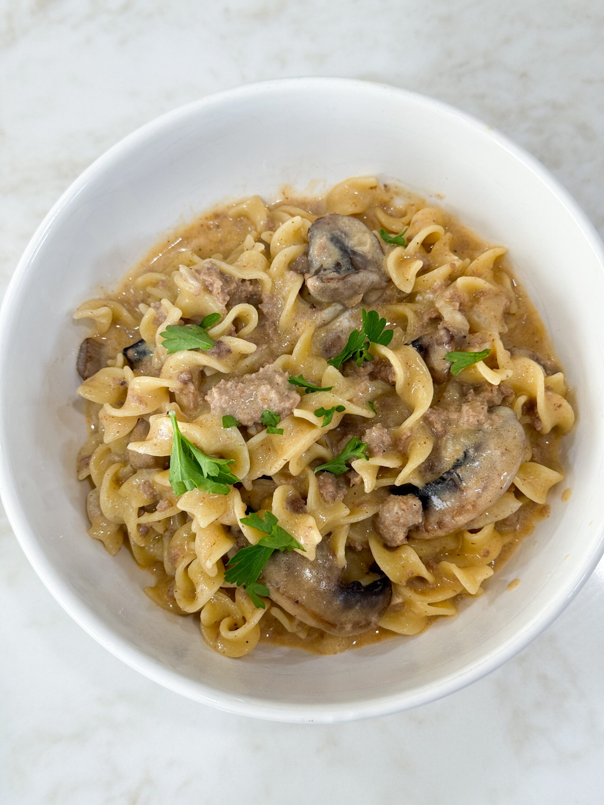 Cooked egg noodles and ground turkey for stroganoff and white bowl