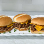 Simple Sloppy Joe sandwiches with cheese on hambuger buns on a long white plate on top of a white counter