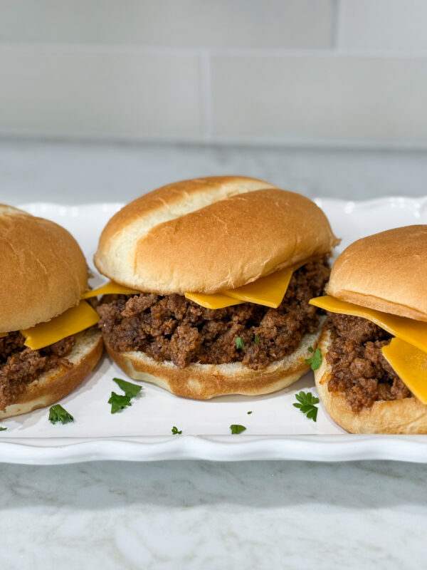 Simple Sloppy Joe sandwiches with cheese on hambuger buns on a long white plate on top of a white counter