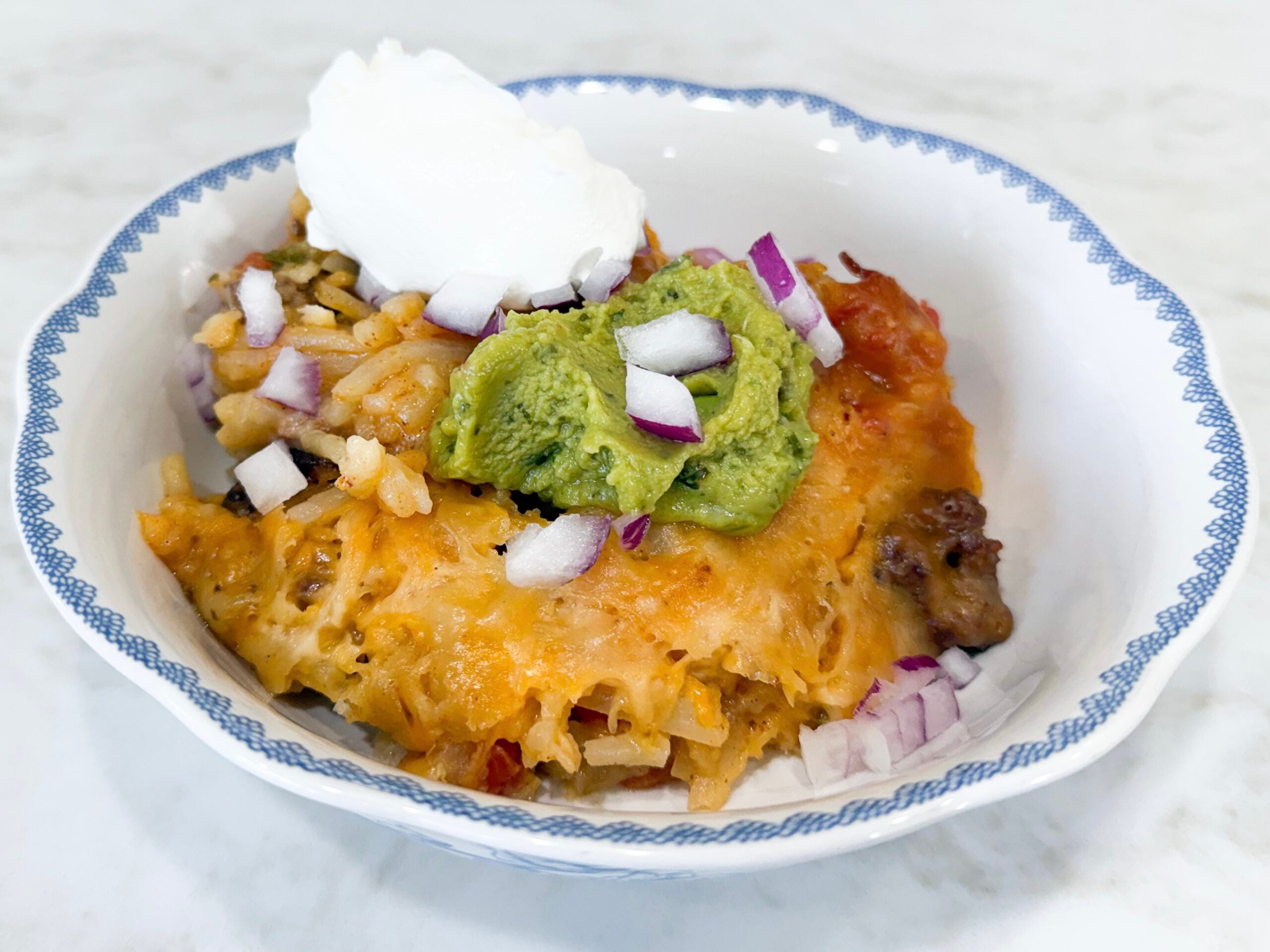 slow cooker potato taco casserole with ground beef, hash browns, cheese, Rotel, and taco toppings in a bowl
