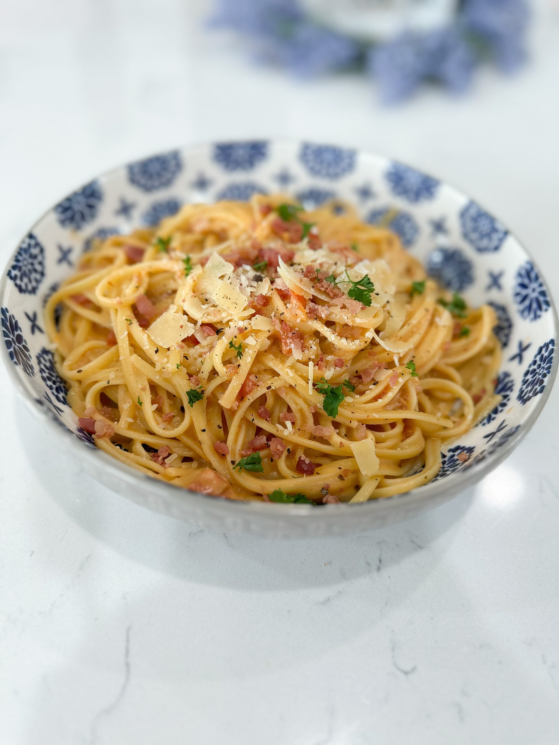Creamy tomato bacon pasta in a white bowl with fettuccine noodles and bacon bits