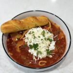 Slow cooker lasagna soup in bowl with spoon and herbs