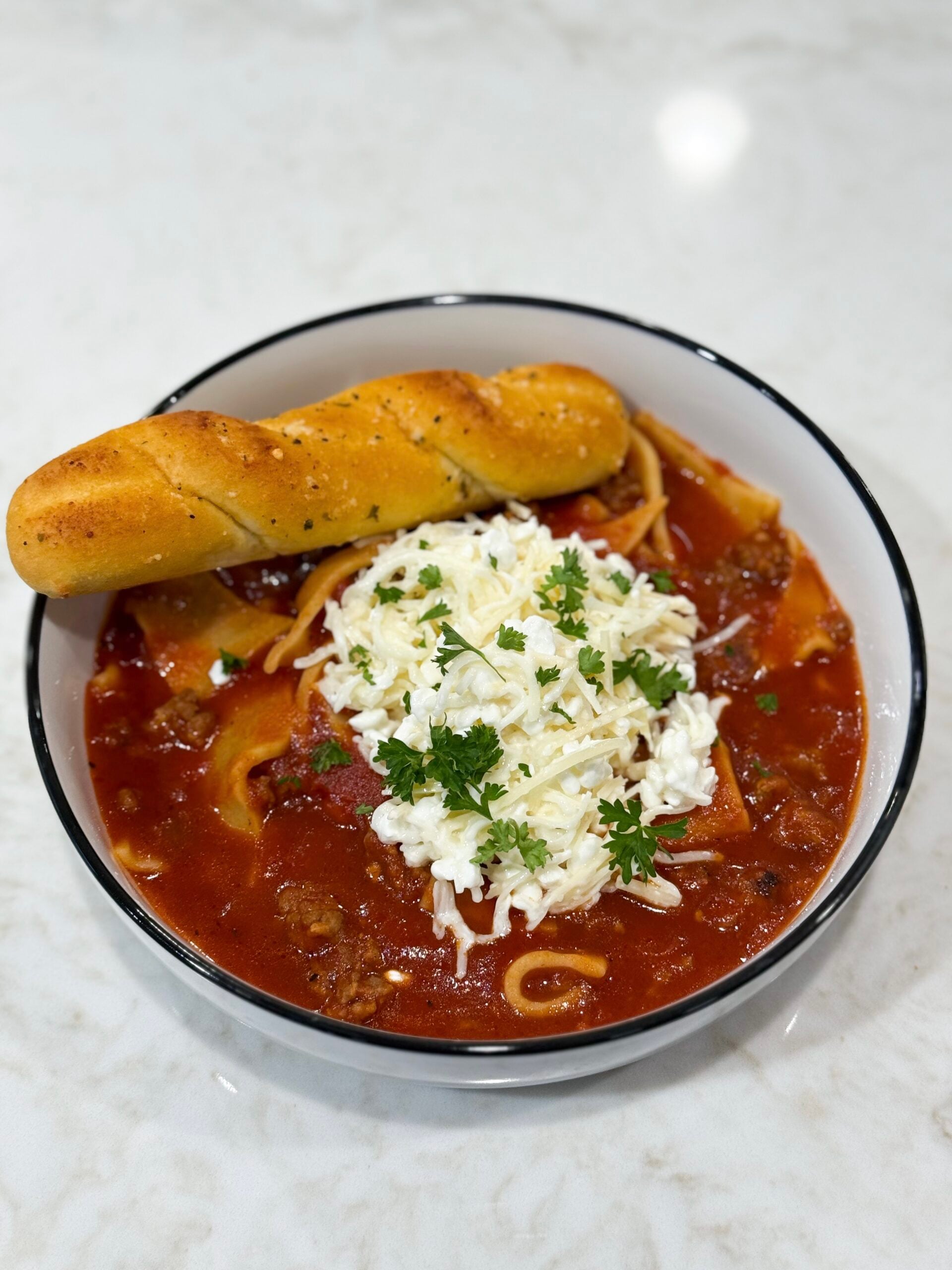 Slow cooker lasagna soup in bowl with with breadsticks and cheese.