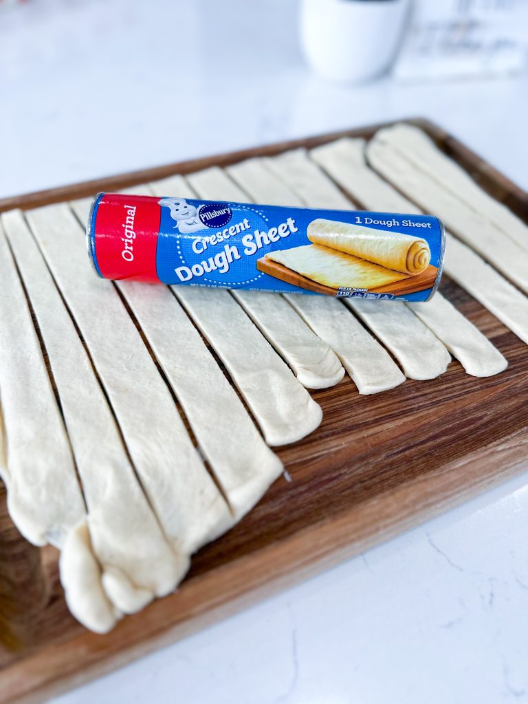 Unrolled crescent dough sheet and cut into strips on a cutting board.