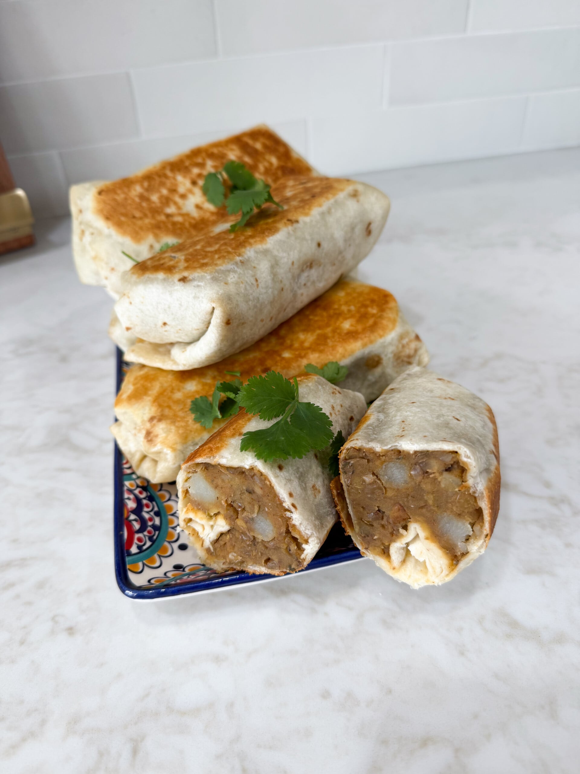 Lentil burritos with potato stacked up on a plate.