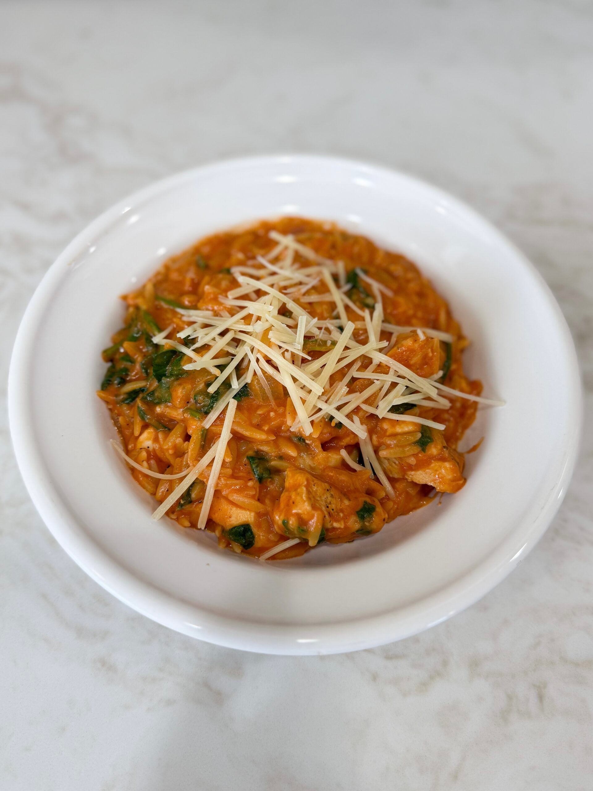 tomato chicken and spinach with orzo in a white bowl topped with Parmesan cheese.