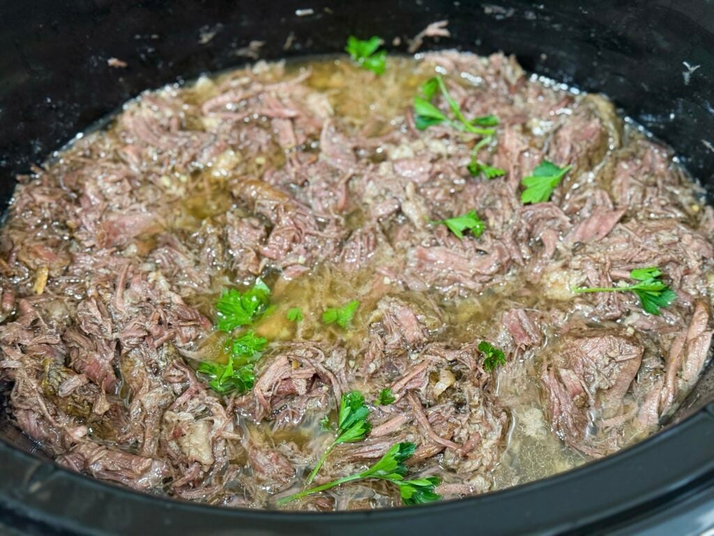 cooked shredded beef in a slow cooker with fresh parsley