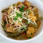 Cooked sausage, potatoes, and beans in a white bowl topped with parmesan cheese and fresh parsley