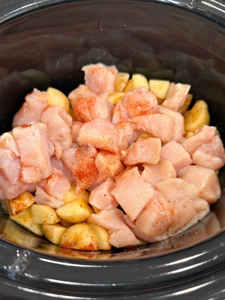 raw chicken and potatoes in slow cooker with seasoning