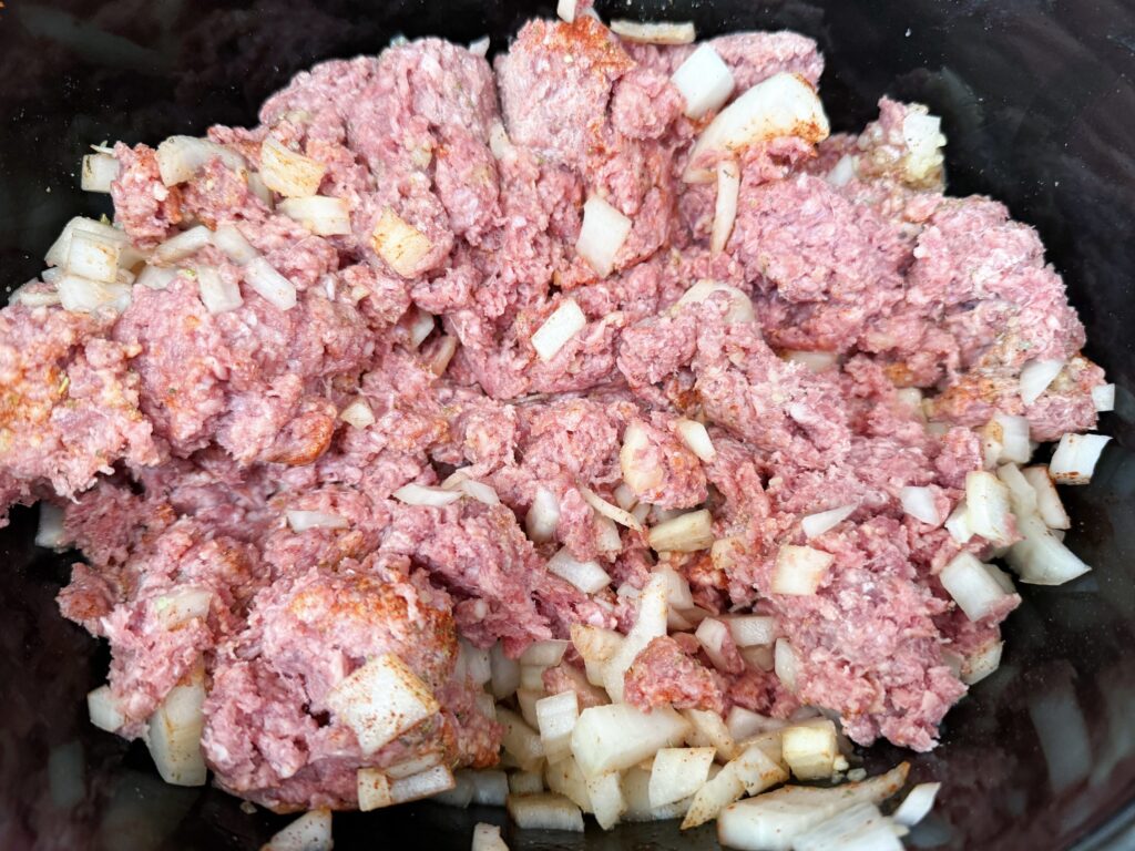 ground beef and onion mixture in a black slow cooker