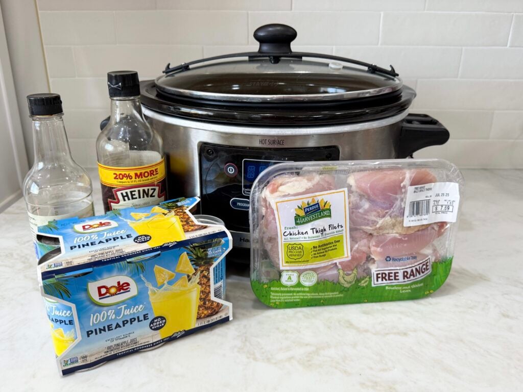 large slow cooker with raw chicken pineapple juice on a white counter