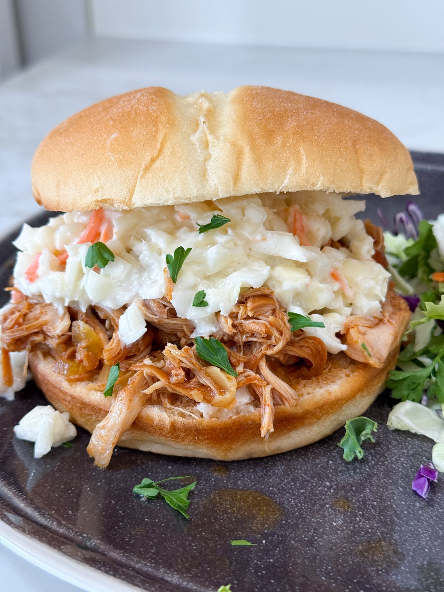 Slow cooker Hawaiian barbecue chicken sandwiches on a black plate with salad on a grey counter