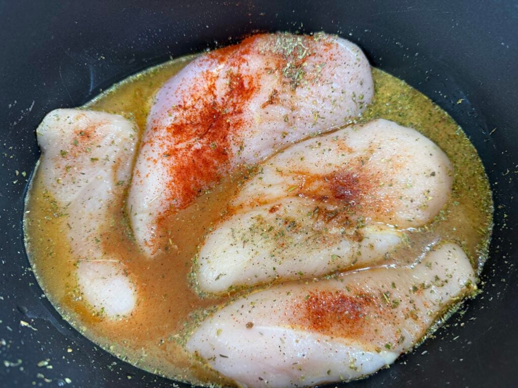 raw chicken with seasoning and broth in a slow cooker