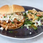 Slow cooker Hawaiian barbecue chicken sandwiches on a black plate with salad on a grey counter
