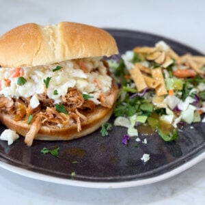 Slow cooker Hawaiian barbecue chicken sandwiches on a black plate with salad on a grey counter
