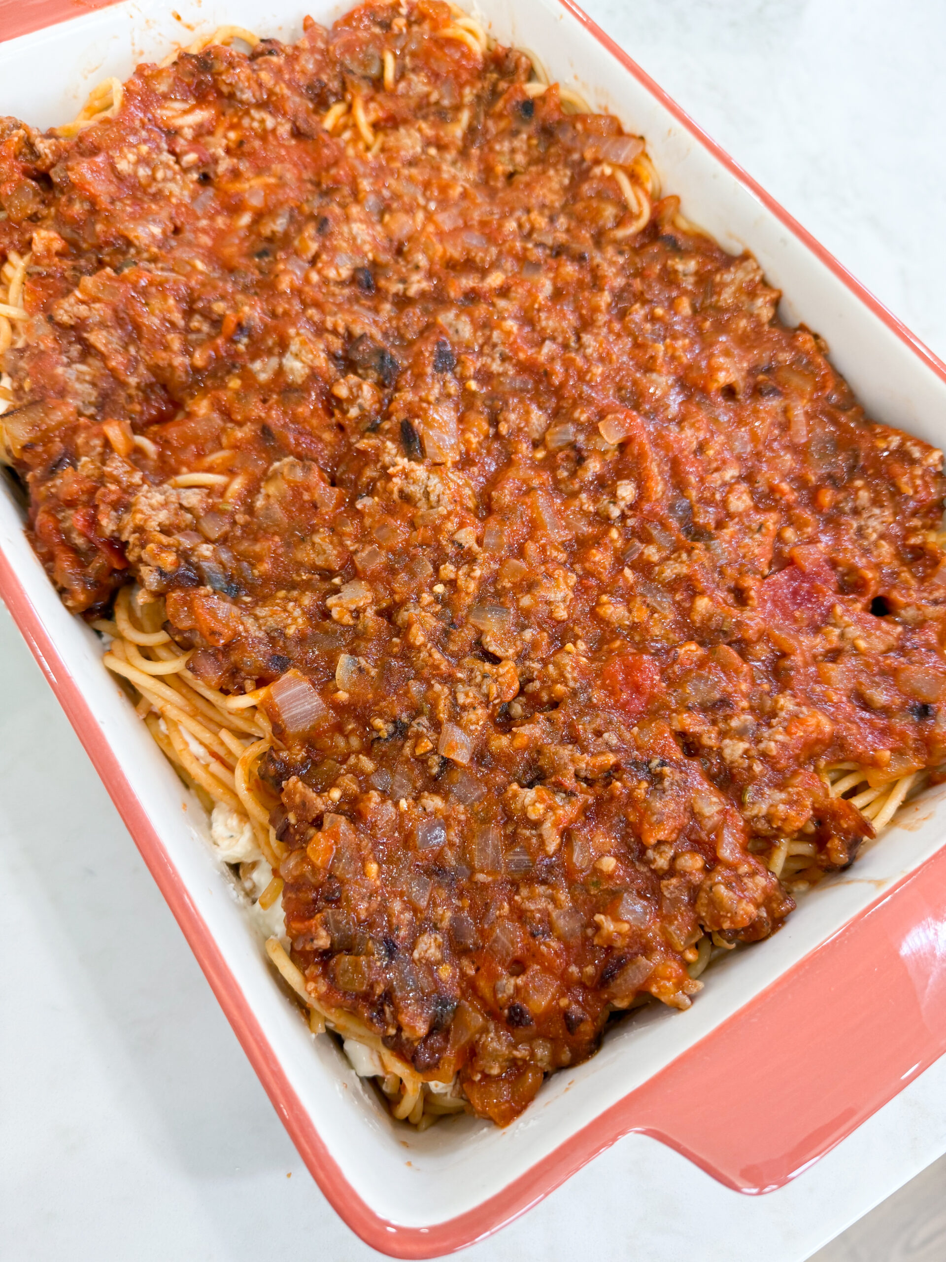 Cooked sausage and marinara mixture spread evenly over spaghetti layers in casserole dish.