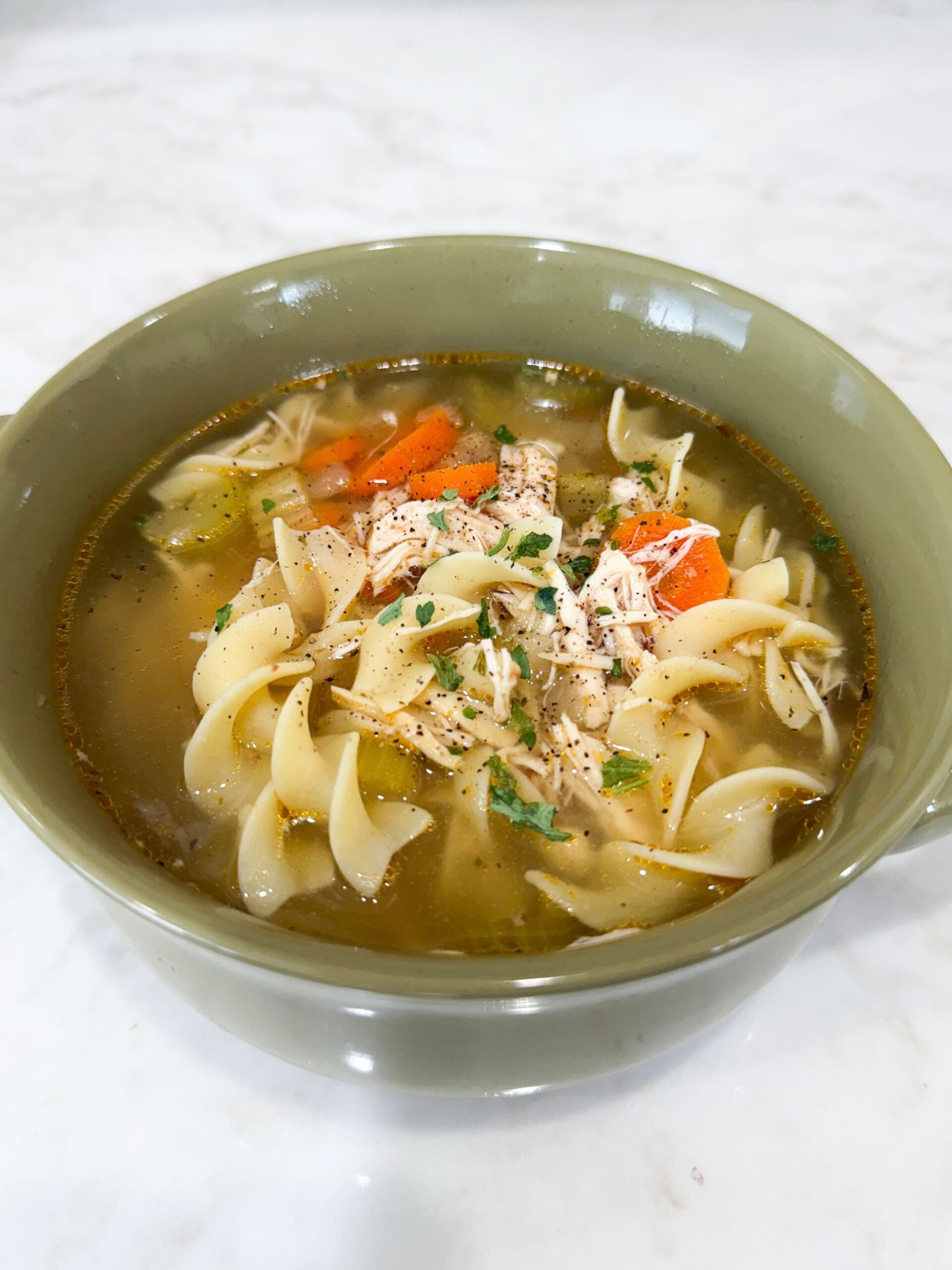 Bowl of Slow Cooker Chicken Noodle Soup with carrots, noodles, and parsley