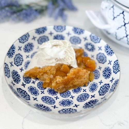 Slow cooker peach cobbler served warm with vanilla ice cream on top
