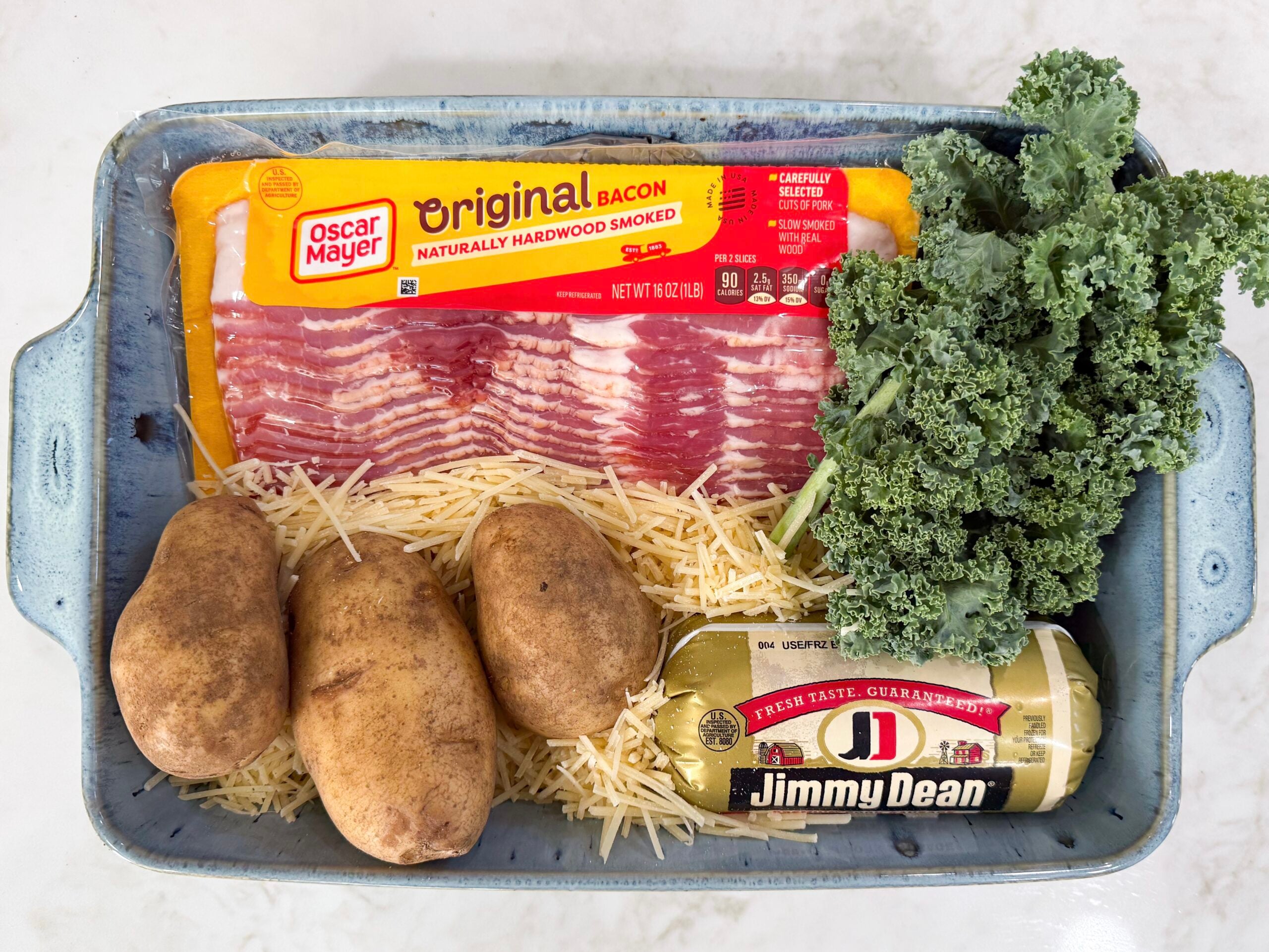 Ingredients for Zuppa Toscana Casserole including potatoes, kale, Italian sausage, bacon, onion, cream, broth, and Parmesan cheese.