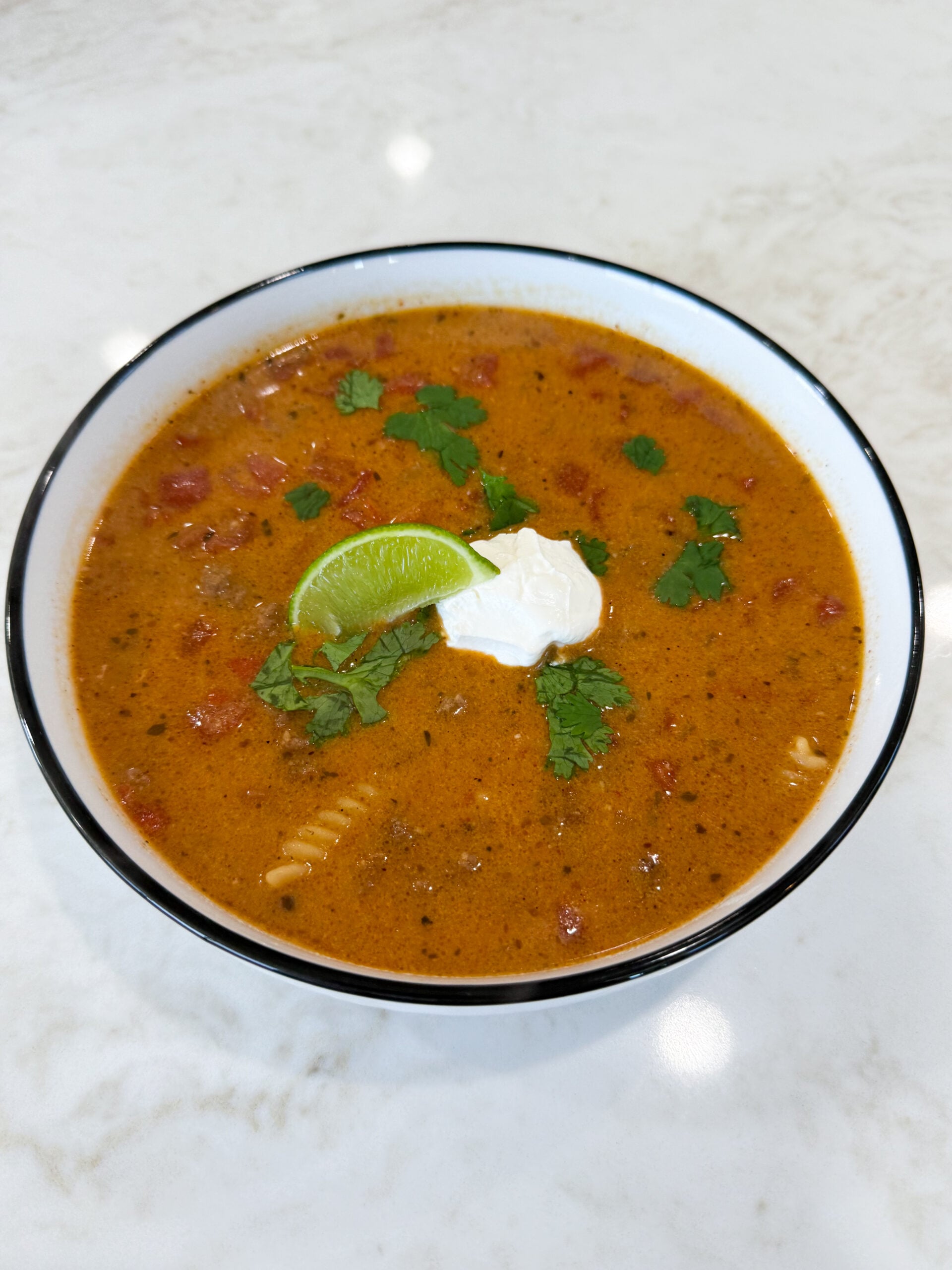 Bowl of cheesy queso chili topped with sour cream, lime, and cilantro