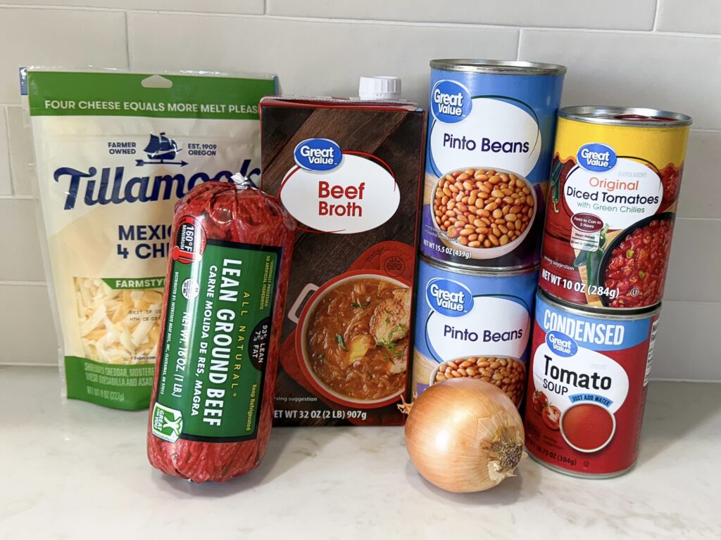 Ingredients for queso chili on counter including ground beef, beans, pasta, and cheese