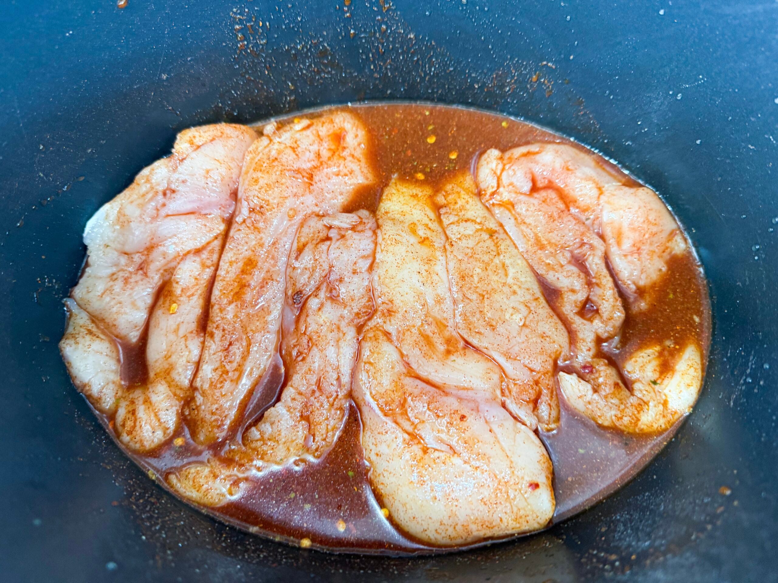raw chicken breasts coated in hot honey sauce inside a slow cooker