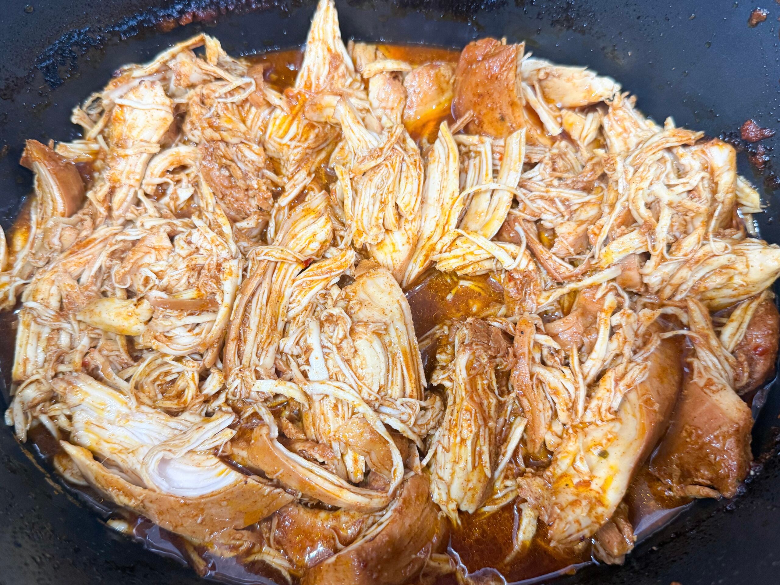 shredded hot honey chicken in a slow cooker coated with sauce