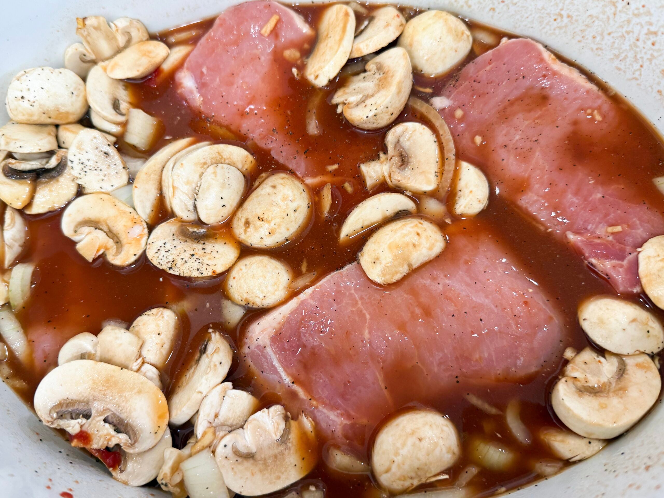 seasoned pork chops arranged on top of onion mushroom mixture in a slow cooker